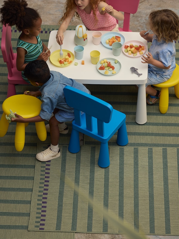 四个孩子坐在MAMMUT MAMMUT儿童桌子椅子,吃的水果。KORSNING地毯在桌子底下。
