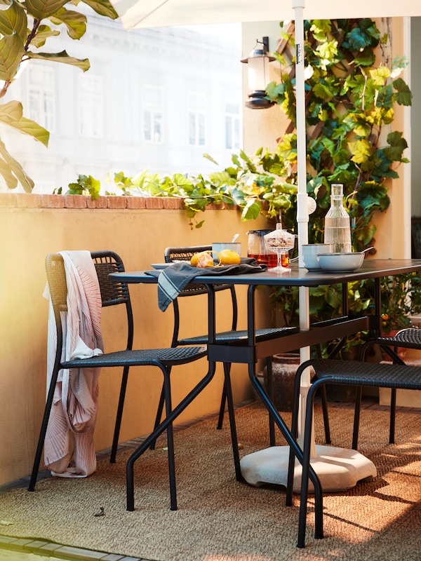 一套深灰色户外餐厅家具在阳台上与水果、茶、水和餐具放在桌子上。