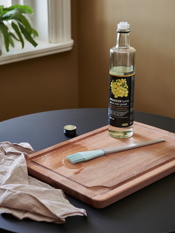 一瓶SMAKRIK菜籽油站在PROPPMATT山毛榉案板放在一个黑色,圆桌。