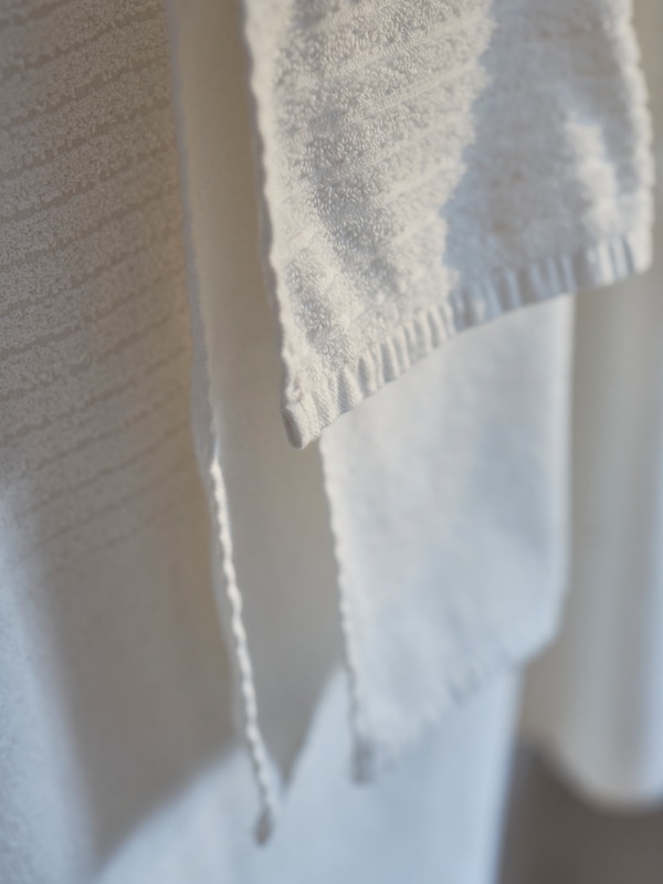 Några vita VÅGSJÖN handdukar med randig vit-på-vit-design hänger från en handduksstång på väggen i ett soligt badrum。