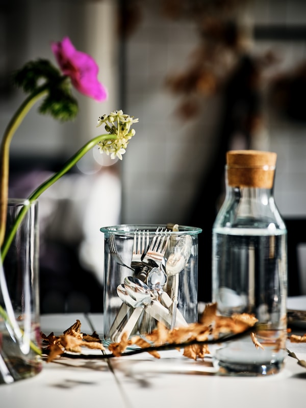 与宜家365 +透明玻璃桌面玻璃水瓶软亚博平台信誉怎么样木,餐具聚集在一个玻璃罐中,和两个花在花瓶里。