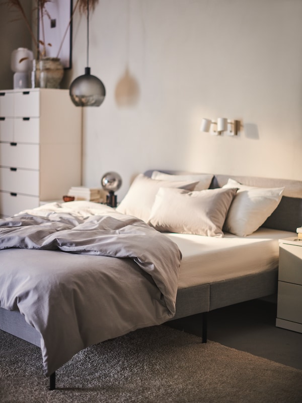一张浅灰色SLATTUM软垫床架，ÅKREHAMN泡沫床垫和NATTSVÄRMARE床上用品靠墙摆放。