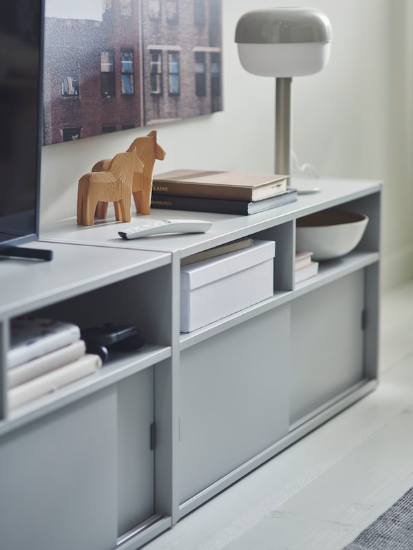 两个浅灰色SPIKSMED电视的长凳上有一个电视装置,遥控器,木马数据,书和一个台灯。