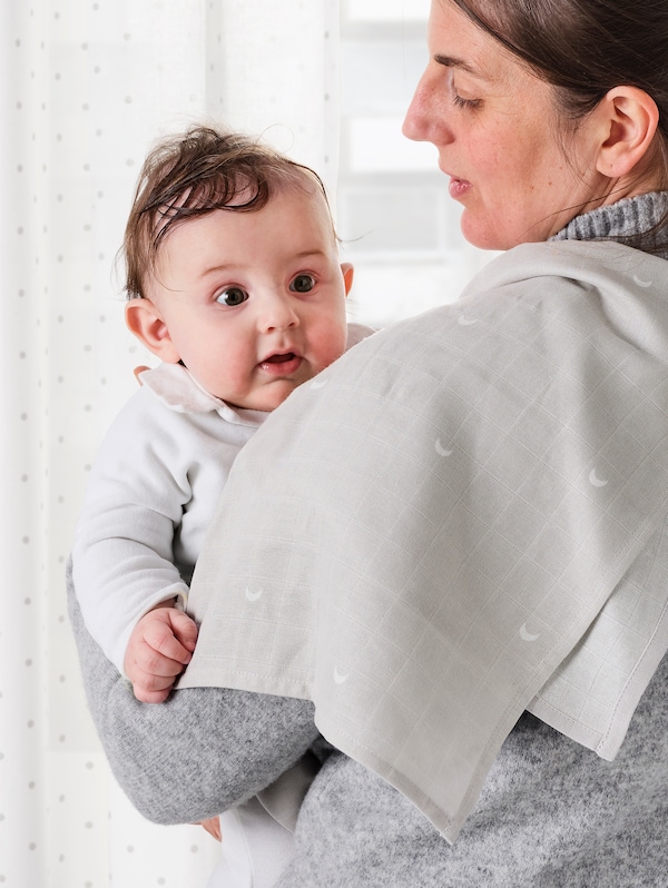 一个女人与一个灰色灰色毛衣LEN棉布与虚线月球模式搭在她的肩膀上,抱着一个婴儿。