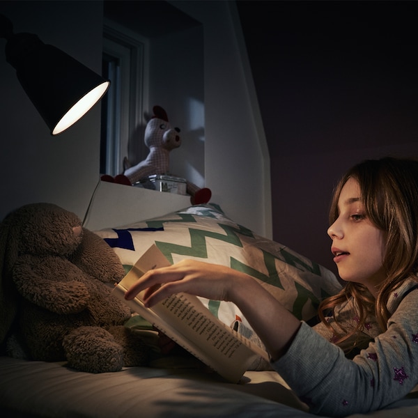 女孩在床上看书连同她的泰迪熊在LED灯泡的灯光。