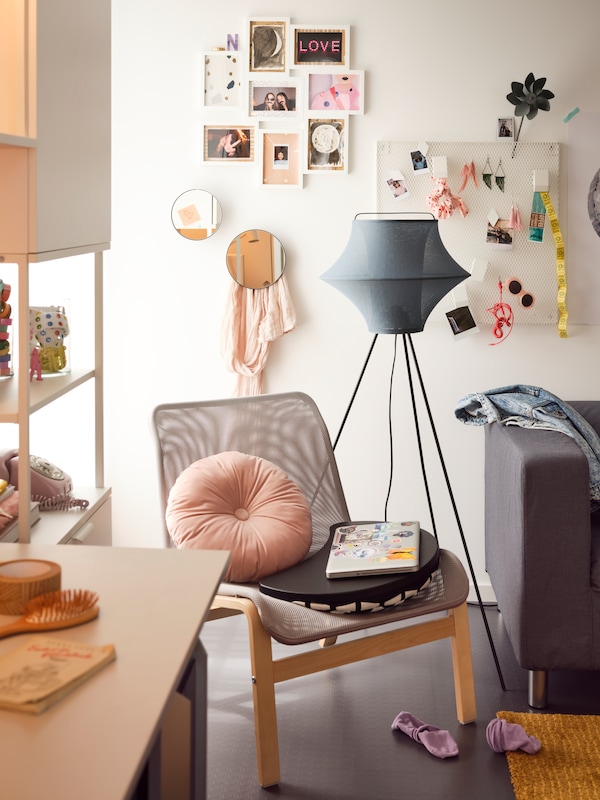 灰色NOLMYRA安乐椅,圆形粉色缓冲的落地灯和墙上的照片。