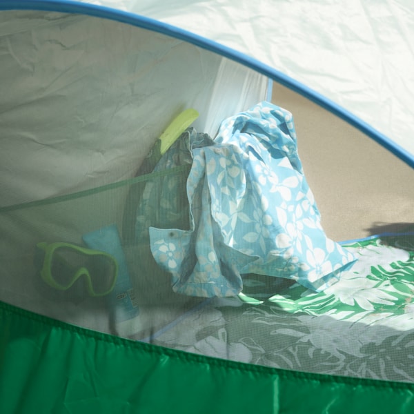 Biało-zielony koc piknikowy STRANDON z motywem liści jest rozłożony wewnątrz zielono-niebieskiego namiotu plażowego STRANDON。