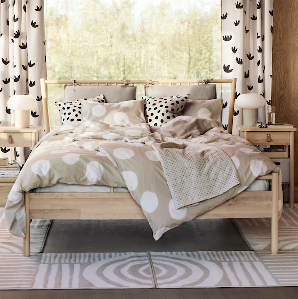 坚实的桦树BJORKSNAS双人床覆盖KLYNNETAG床单和点模式。两个VEJSTRUP地毯在地板上。