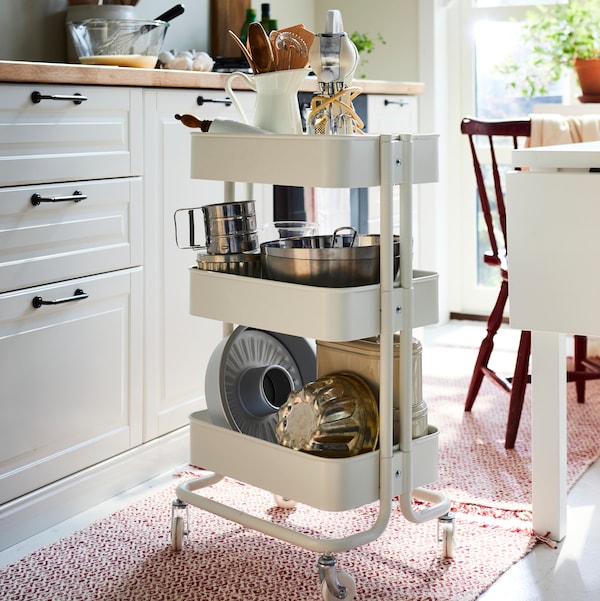 白色的厨房与RASKOG厨房手推车的书架上放满了锅,锅,和一个IDEALISK筛。