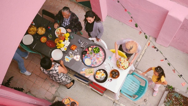 狭窄的庭院与粉红色的墙壁和所有年龄段的人都在一个长桌上提供食物和鲜花OMSESIDIG台布。