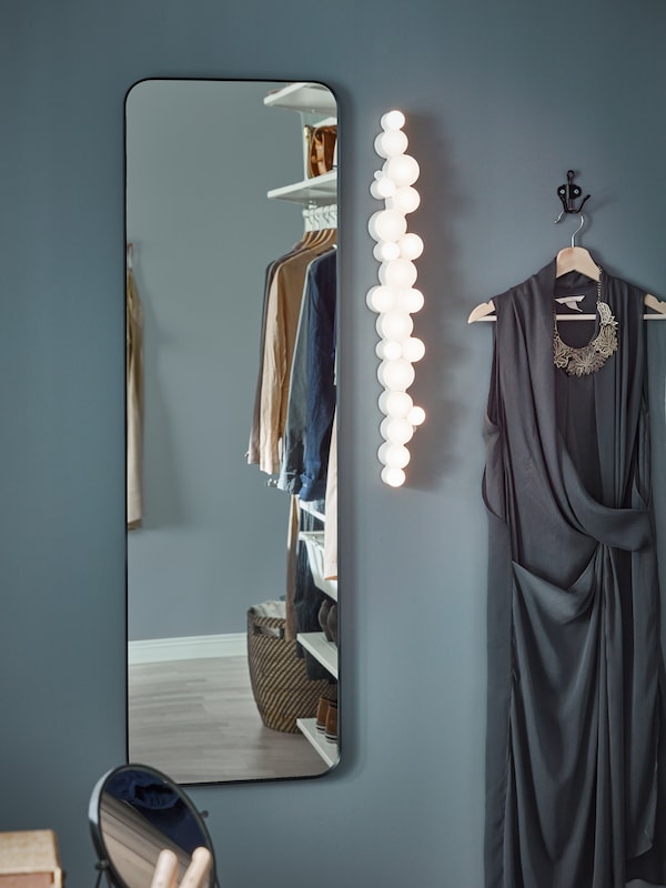 LINDBYN镜子安装在一个黑暗的蓝色的墙。旁边是一个LED壁灯和钩上的灰色的晚礼服。