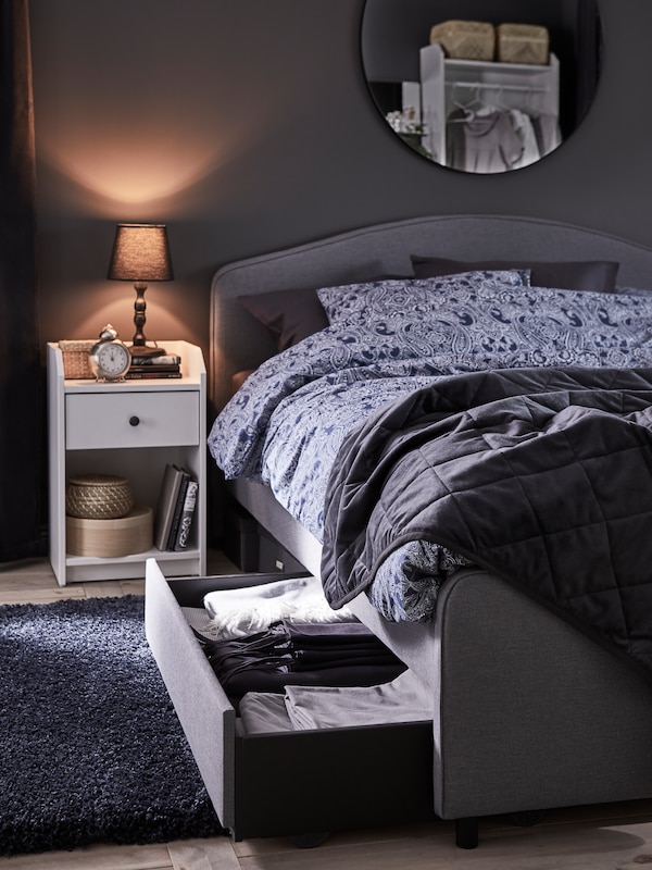灰色HAUGA存储抽屉拉出软垫床,和一个床头柜旁边拿着一个小台灯。