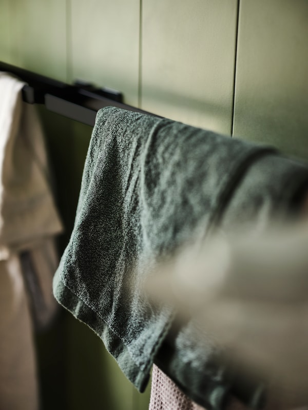 Einige Handtucher, darunter静脉dunkelgrun-meliertes Badetuch冯·HIMLEAN hangen uber einem schwarzen SKOGSVIKEN-Handtuchhalter。