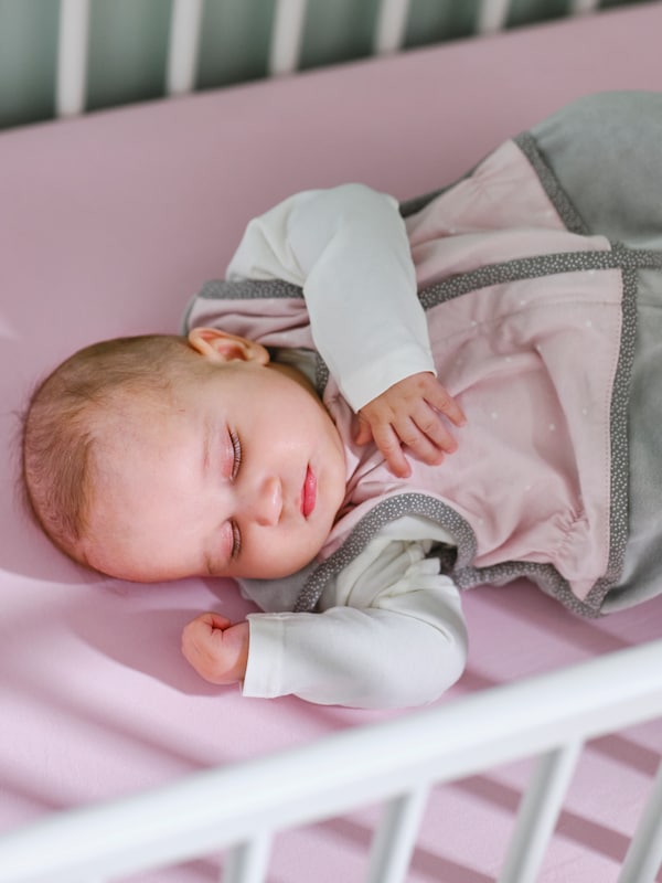 婴儿在一个粉红色的LEN睡眠包放在一张粉红色的LEN安装格列佛在一个白色的床睡着了。