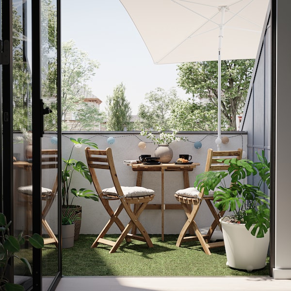 阳台上有两个木制椅子和桌子在ASKHOLMEN系列,加上grey-beige阳伞和各种盆栽。