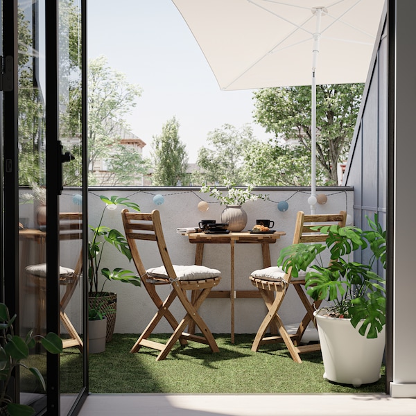 阳台上有两个木制椅子和桌子在ASKHOLMEN系列,加上grey-beige阳伞和各种盆栽。