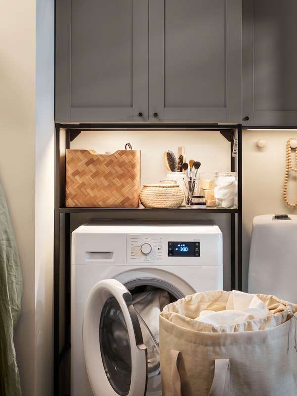 浴室洗衣房，带有灰色enet正面的储物柜，UDDARP洗衣机/烘干机组合和架子上的浴室用品。