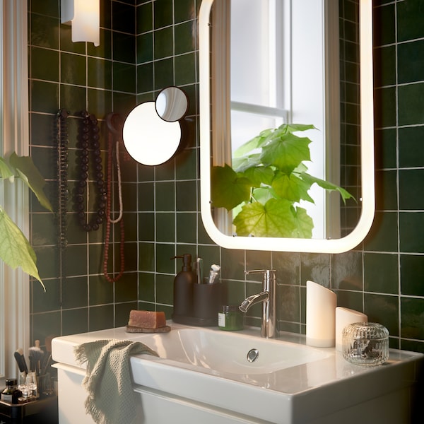 一个浴室和一个白镜综合照明猛然站起身,加上亮绿色的客人的毛巾,旁边还有一盆植物。