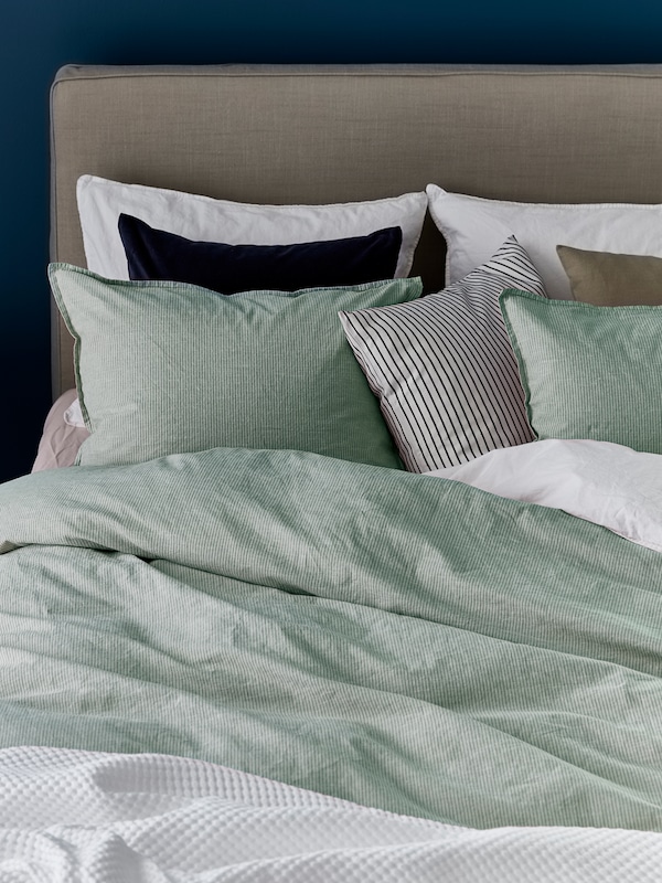 床的床头板,枕头与白色、黑色和绿色枕套和BERGPALM被套与绿色的细条纹。
