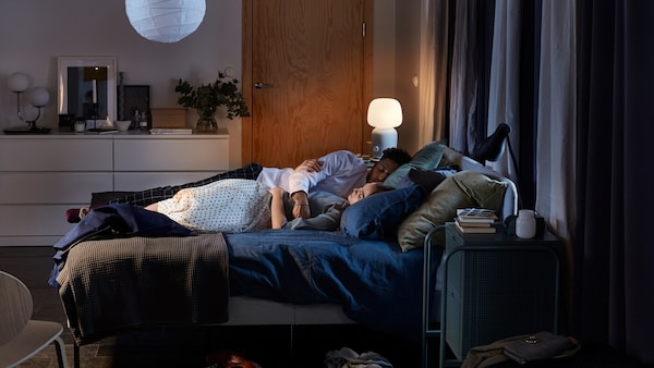 卧室与SLATTUM软垫床框,两个灯和深蓝色的棉被覆盖,睡在床上。