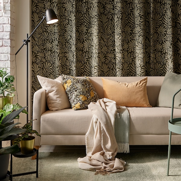 浅褐色LINANAS光灰绿色的地毯沙发与各种靠垫,前面的树叶图案的窗帘挂在墙上。
