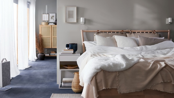 桦树BJORKSNAS床上用白色和米色床用织物在白色的床头柜,竹台灯和一个空气净化器。