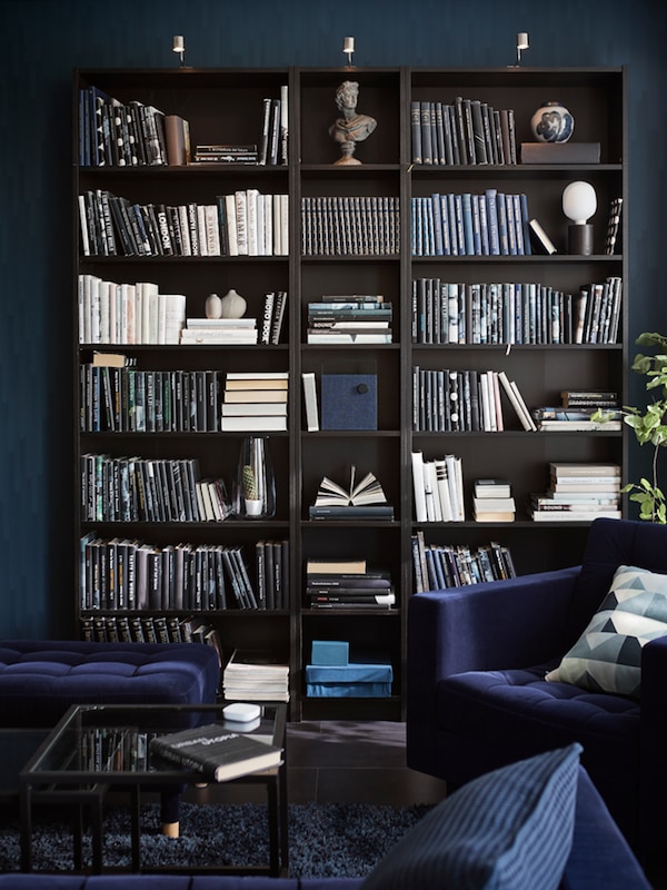 黑褐色比利书柜在蓝色客厅充满了大量的书籍和一些对象。一个蓝色的扶手椅是在前面。