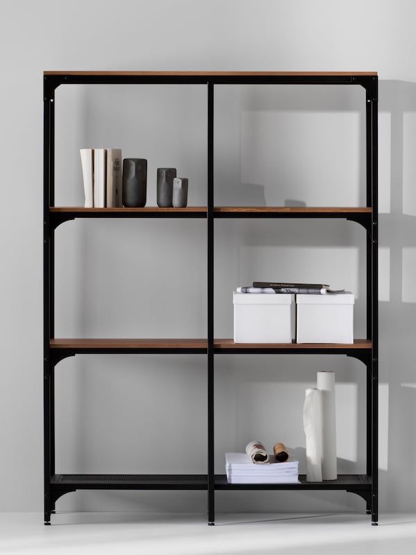 黑色FJALLBO搁置单元对一个灰色的墙。书架上有两个盒子,一些书籍和装饰品的集合。