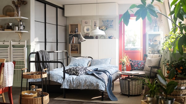 黑色FYRESDAL床与两个床垫SOMMARSLOJA床单站在一间小公寓里。