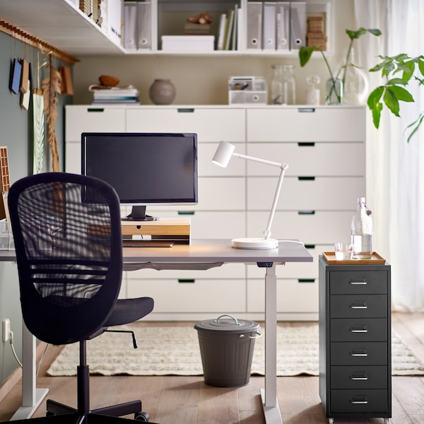 黑色办公椅和赫尔默抽屉单元由一个灰色/白色RODULF坐/站桌子一个工作灯和电脑屏幕。