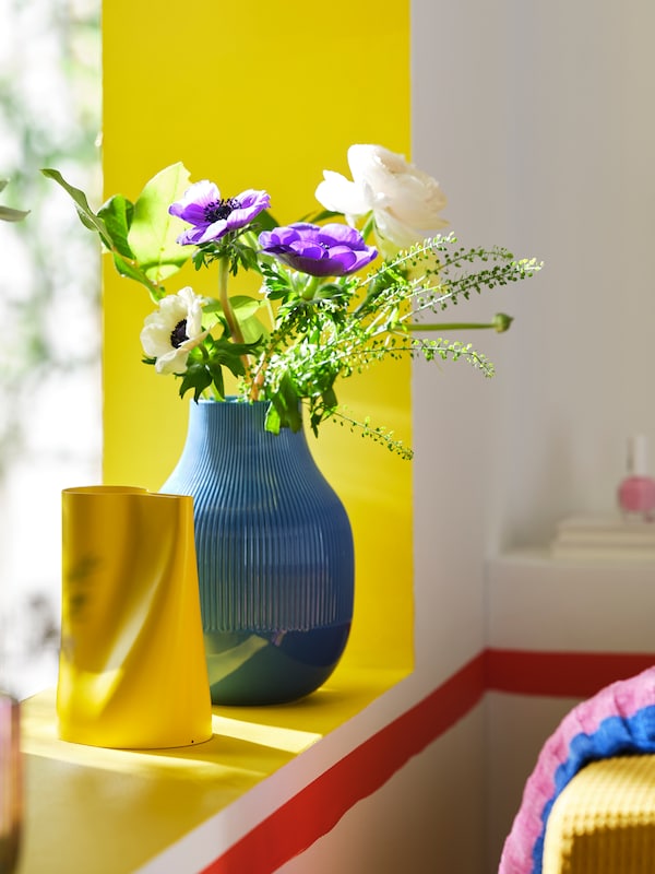 蓝色GRADVIS鲜花的花瓶和一个明亮的黄色CHILIFRUKT花瓶,都放在一个黄色的窗台。