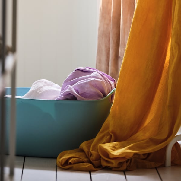 一个蓝色TORKIS洗衣篮站在旁边的地板上五颜六色的窗帘。