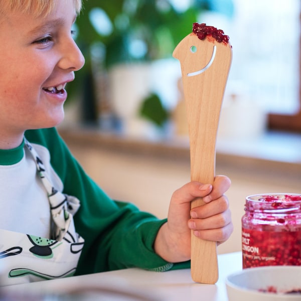 一个男孩有一个木制UPPLIVAD勺子抹与SYLT LINGON传播在厨房台面、勺子笑脸断路器。