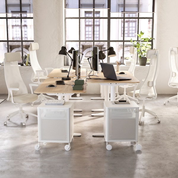 明亮的开放式办公室有四个BEKANT桌子集群中的每一个都有白色办公椅和黑色工作灯。