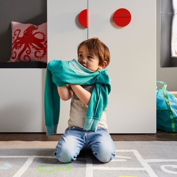 一个孩子穿衣服灰色地毯的白色的长椅上与玩具存储和一个白色的衣柜撤出单位。