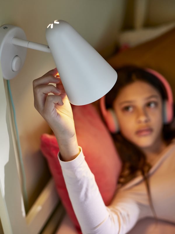 孩子与粉红色耳机倚靠着粉红色垫调整上面挂着一台白色FUBBLA LED壁灯。