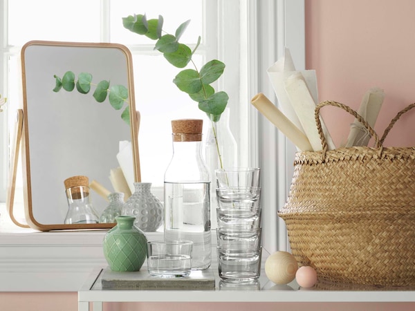 家居装饰项目的集合,包括一面镜子,花瓶、小戴眼镜玻璃玻璃水瓶,一篮子都坐在一个窗口一个粉红色的墙上。