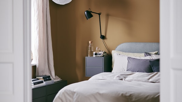 一个舒适的卧室用丰富的焦糖的墙和VADHEIM软垫床框架,一个壁灯和一个床头柜。