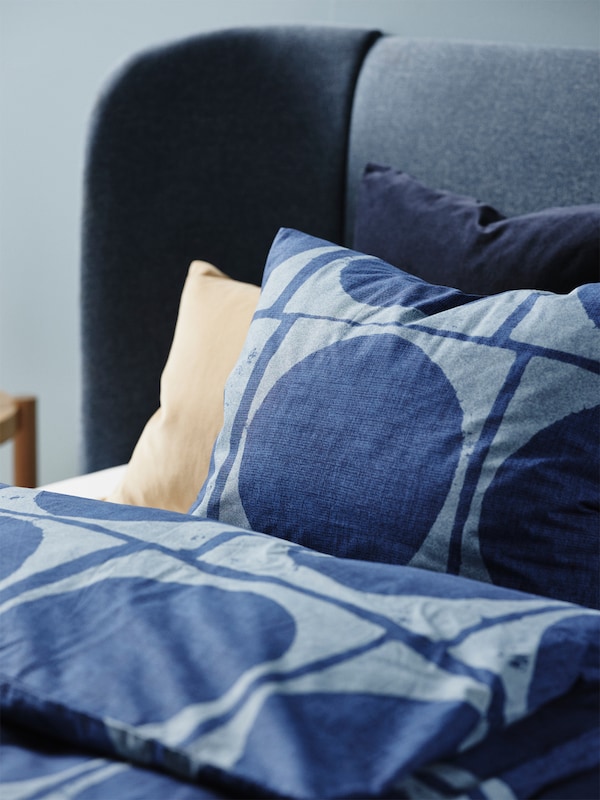 深蓝色JORDRANUNKEL枕套,被套在一个床上。米色和蓝色枕头支撑背后主要的枕头。