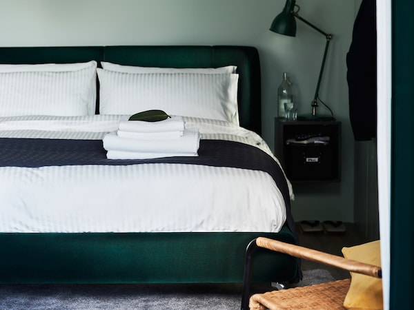 与NATTJASMIN深绿色TUFJORD软垫床床单站在卧室与绿色的墙。