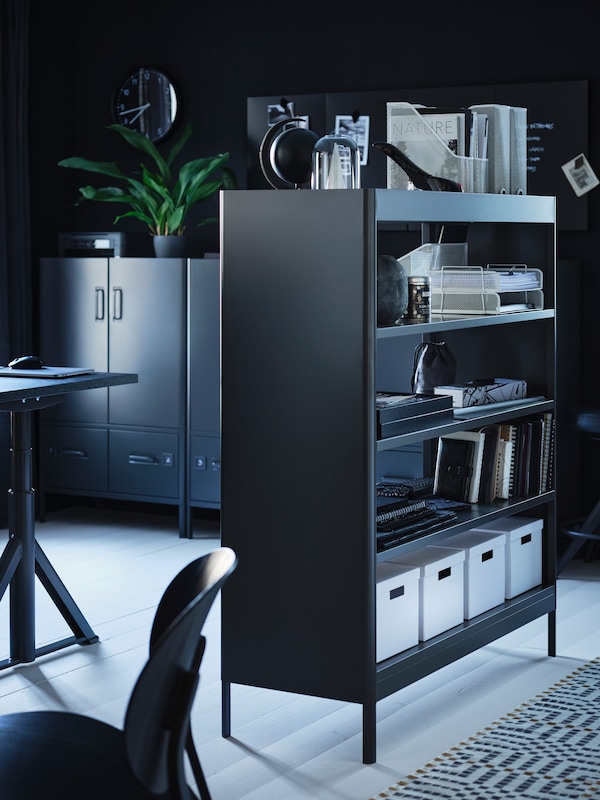 一种深灰色的IDÅSEN置物架，用作家庭工作空间的房间分隔物，用来放置储物箱、书籍和其他物品。