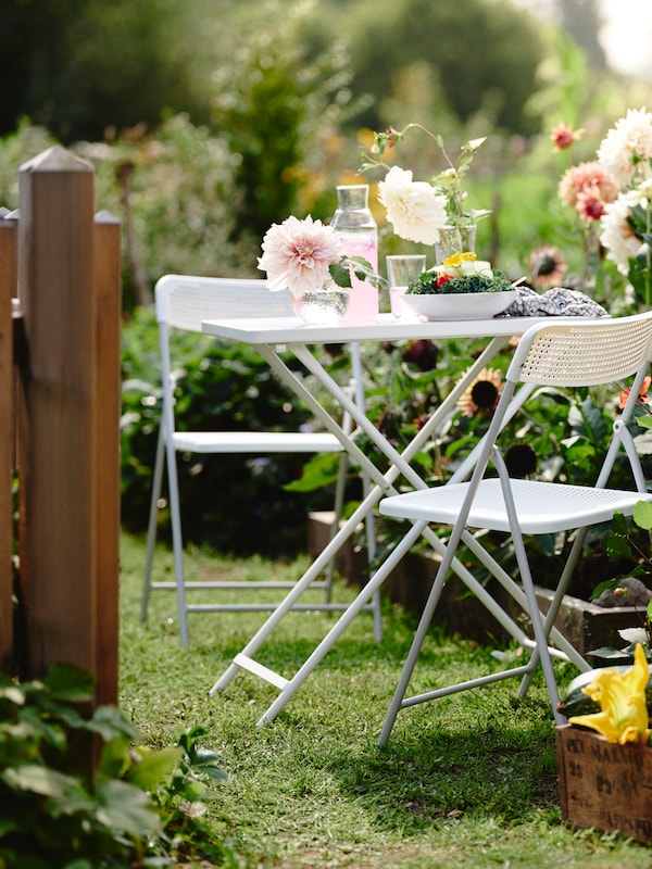 一个华丽的户外花园有两个TORPARO椅子和TORPARO表粉红色饮料,花瓶和一个沙拉盘。