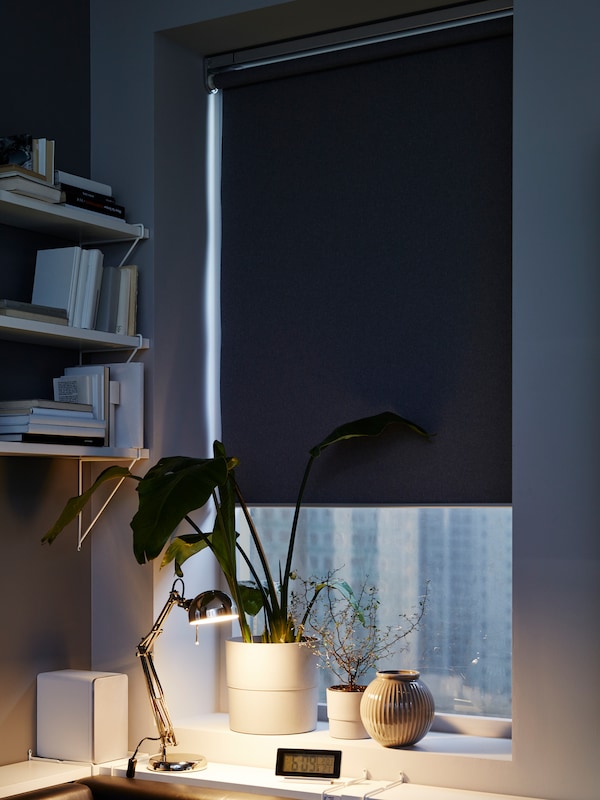 一个FYRTUR阻挡遮光窗帘覆盖大多数窗口,盆栽植物和窗台上的花瓶,白墙的货架上。