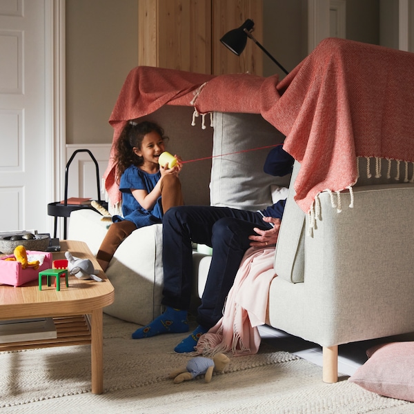 一个女孩和一个男人在一个毯子堡建立在米色PARUP沙发,旁边一棵橡树单板咖啡桌米色地毯。