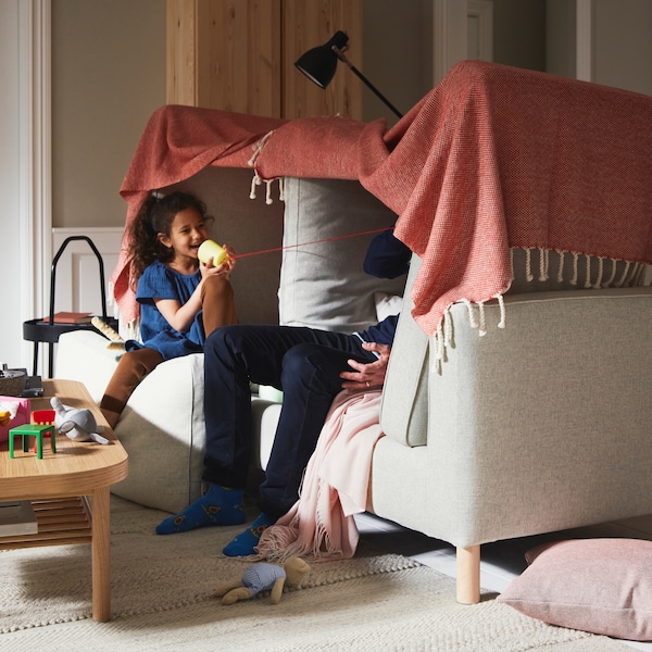 一个女孩和一个男人在一个毯子堡建立在米色PARUP沙发,旁边一棵橡树单板咖啡桌米色地毯。