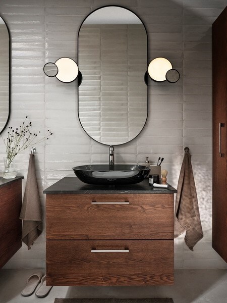 一个GODMORGON盥洗台和两个抽屉和一个OXMYREN台面脸盆在深灰色玻璃和镜子,毛巾挂。