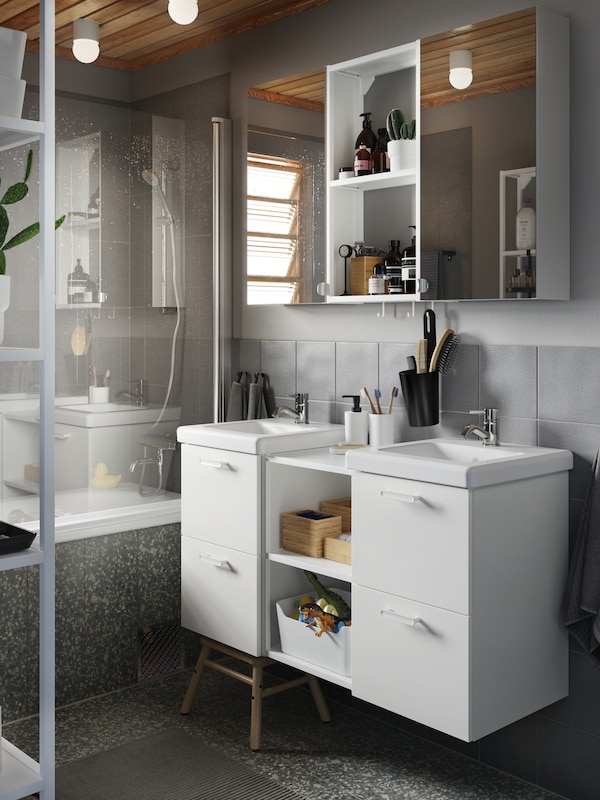一间灰色的浴室，有两个白色的脸盆，两个带镜子门的壁柜，还有浴巾和灰色的浴垫。