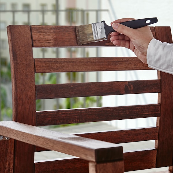 一只手拿着刷子和瓦尔达木材着色剂应用到木制的扶手椅。