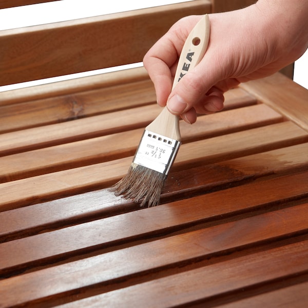 一只手拿着画笔VARDA木材着色剂应用到一块户外家具的表面。