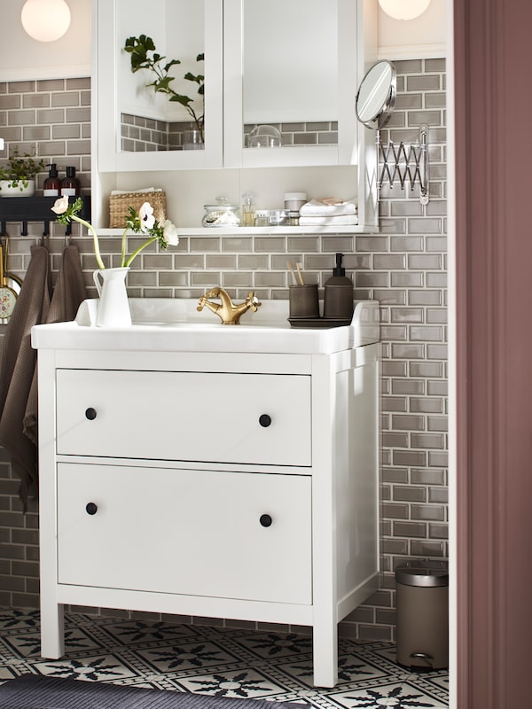 一个白色的HEMNES镜子柜，架子上有浴室用品，一个HEMNES/RÄTTVIKEN洗手台，两个白色抽屉。